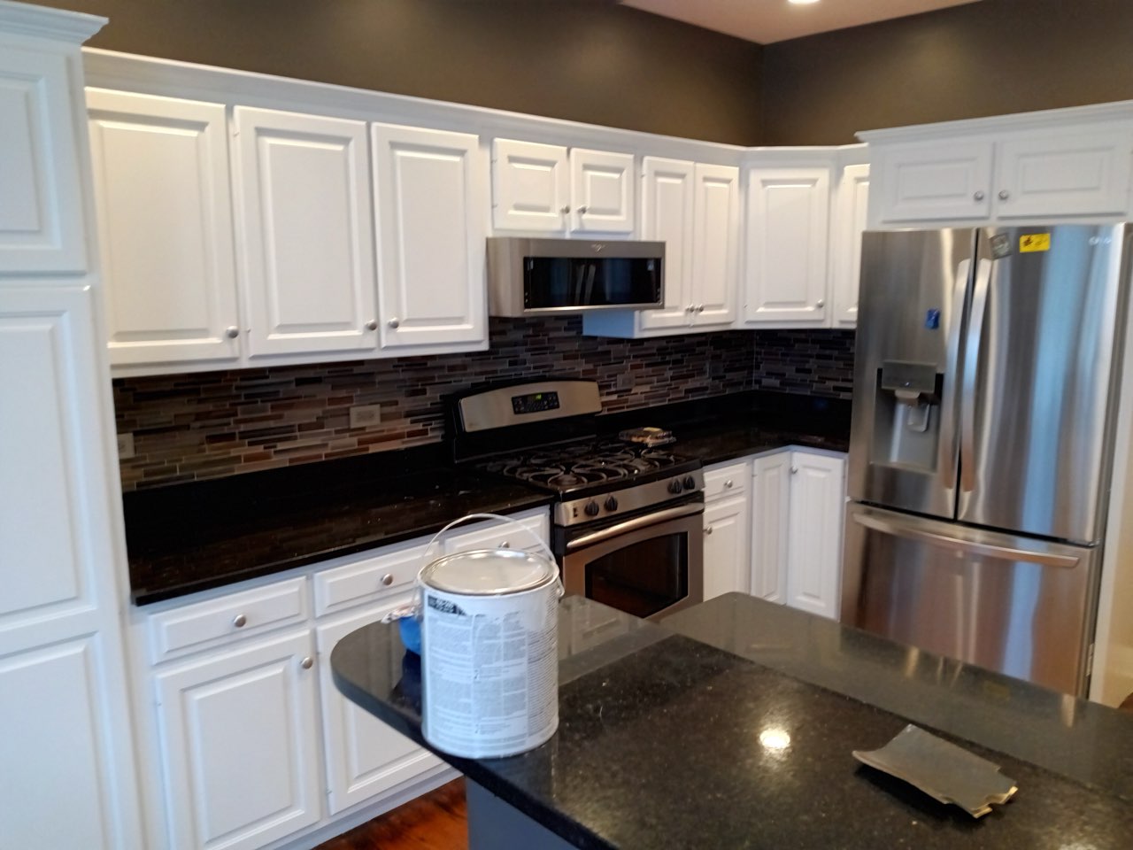 Modern kitchen with white cabinets, black countertops, stainless steel appliances, and brick backsplash