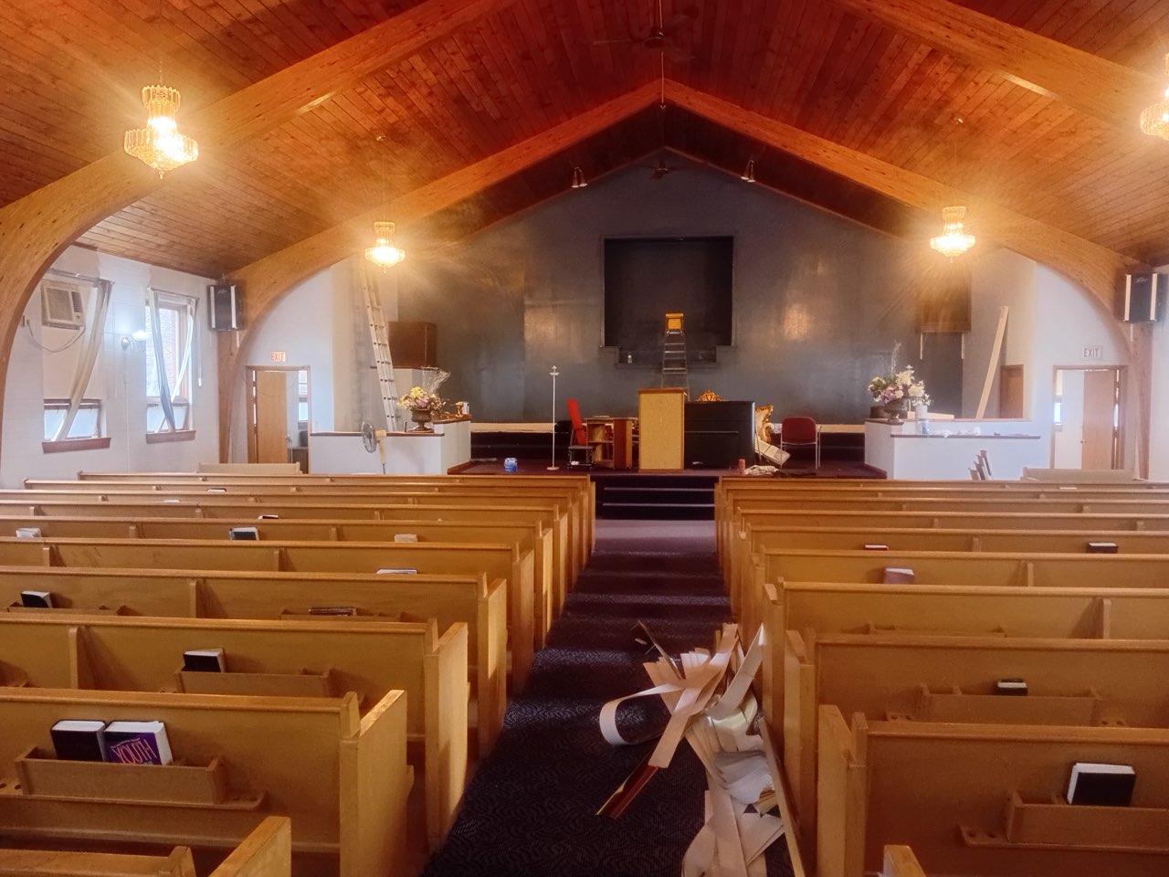 Interior of a wooden church sanctuary with pews, altar, and vaulted ceiling with chandeliers