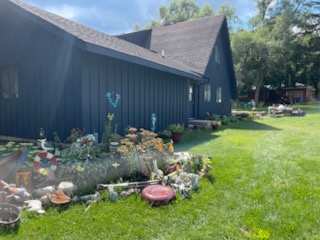 Modern dark cabin with sloped roof, manicured lawn, and colorful flower garden