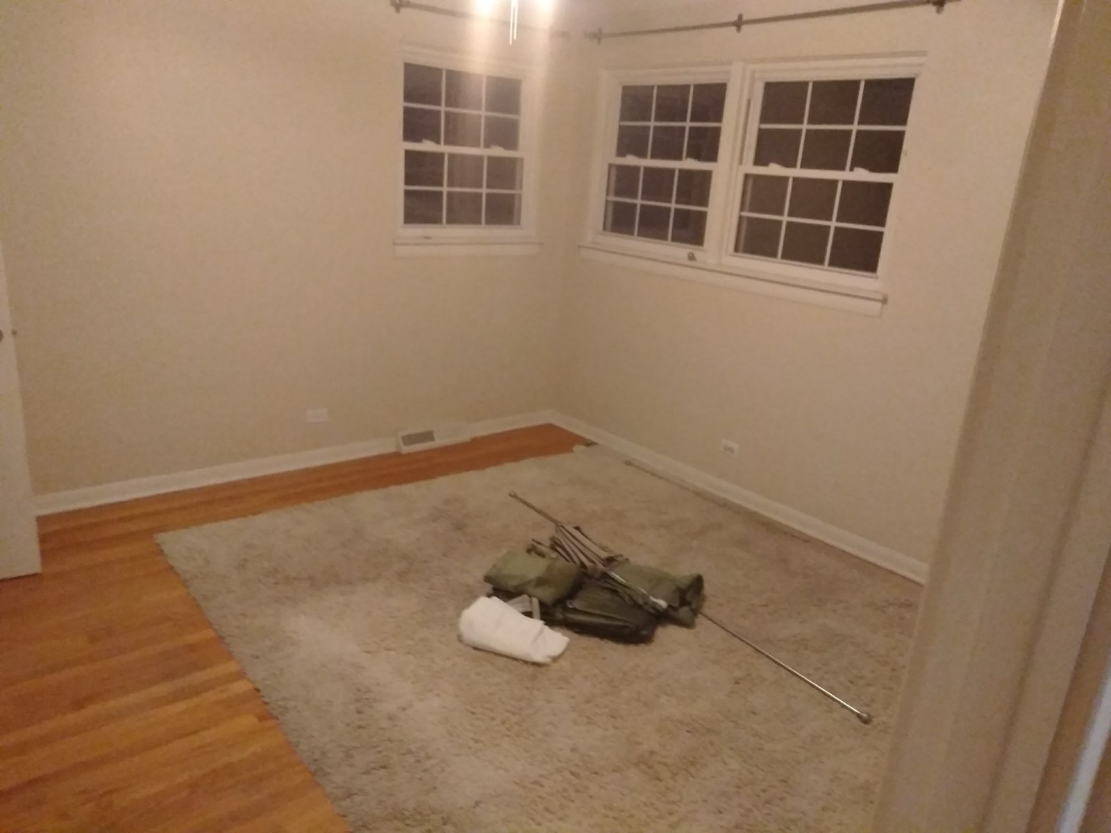 Empty room with wooden and carpeted flooring, white walls, windows, and construction materials on carpet